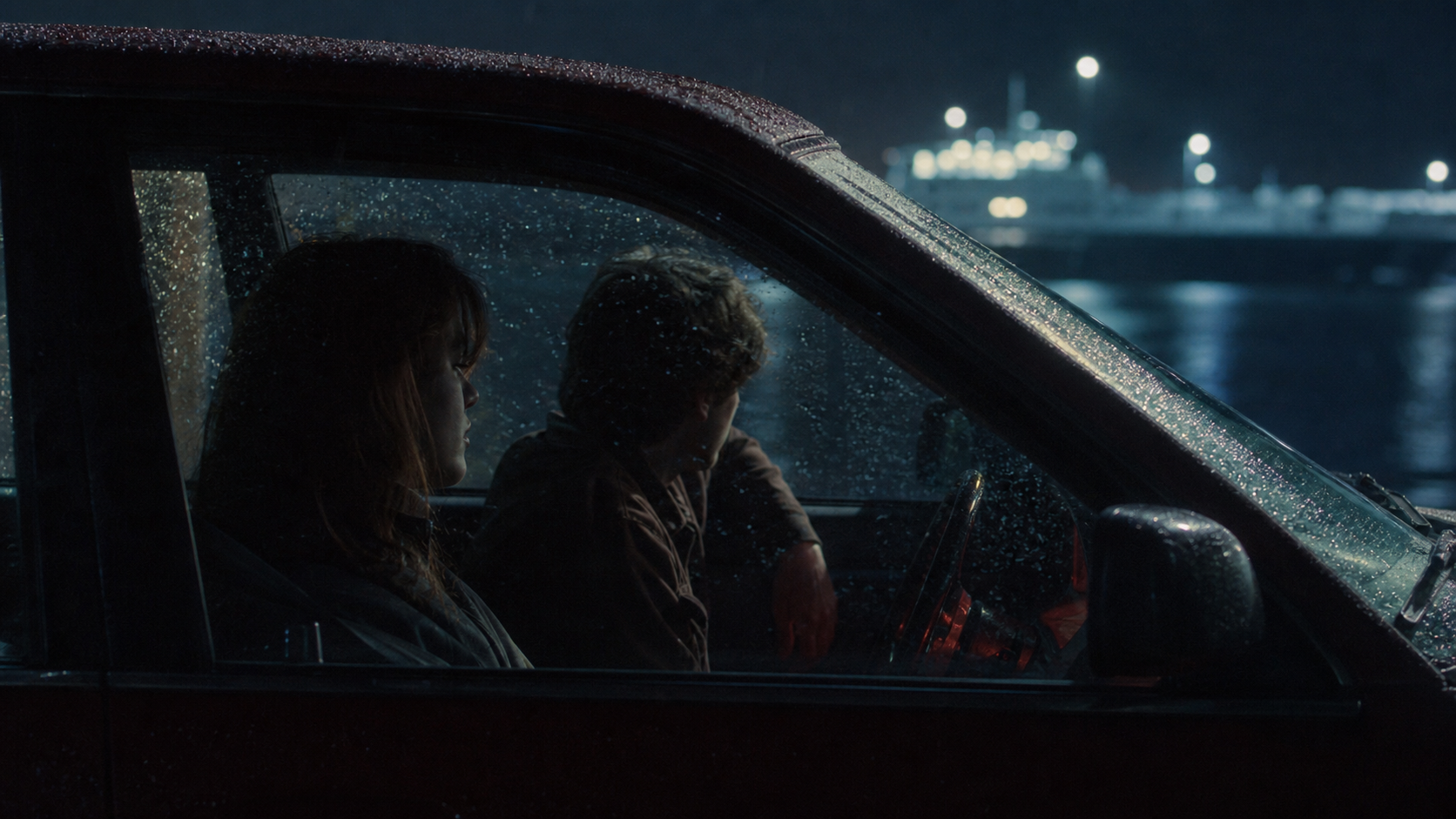 Two people sitting in a rain-covered car near a ferry terminal